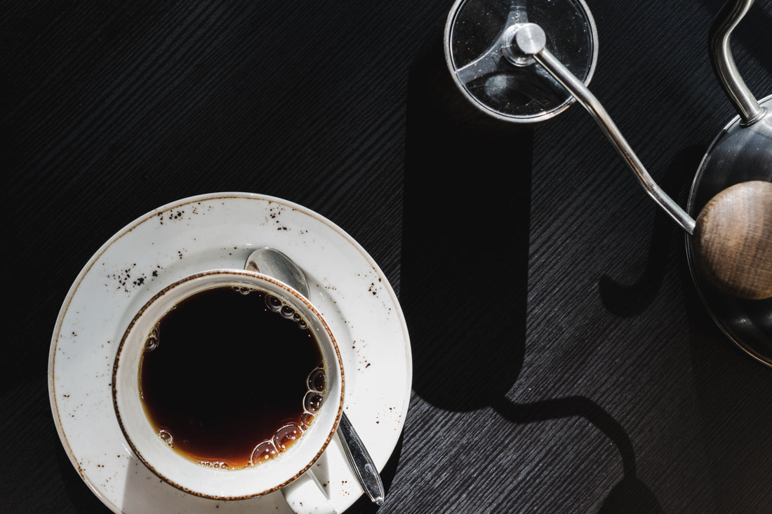 En rykande kopp nybryggt kaffe bredvid en manuell handkvarn..